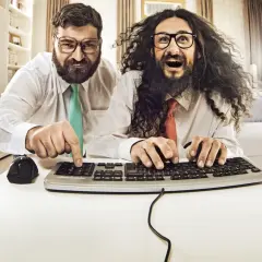 Zwei Männer mit Brillen und Krawatten tippen auf einer Tastatur.