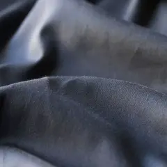 Dunkler, zerknitterter Stoff, der die Nachteile von Polyester wie Knitterbildung und mangelnde Atmungsaktivität verdeutlicht.
