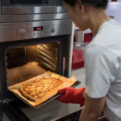 Frau holt goldbraune Pizza aus dem Ofen, der auf Ober-/Unterhitze und Umluft eingestellt ist.