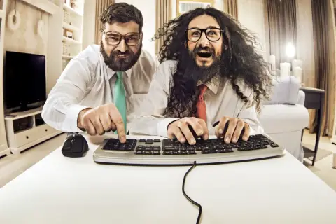Zwei Männer mit Brillen und Krawatten tippen auf einer Tastatur.