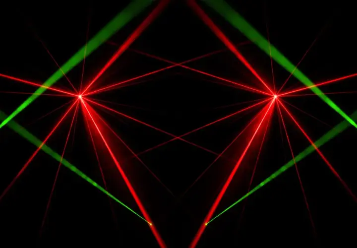 Rote und grüne Laserstrahlen kreuzen sich auf schwarzem Hintergrund. Das Bild zeigt, wie funktioniert ein laser, mit fokussierten Lichtpunkten und ausstrahlenden Strahlen.