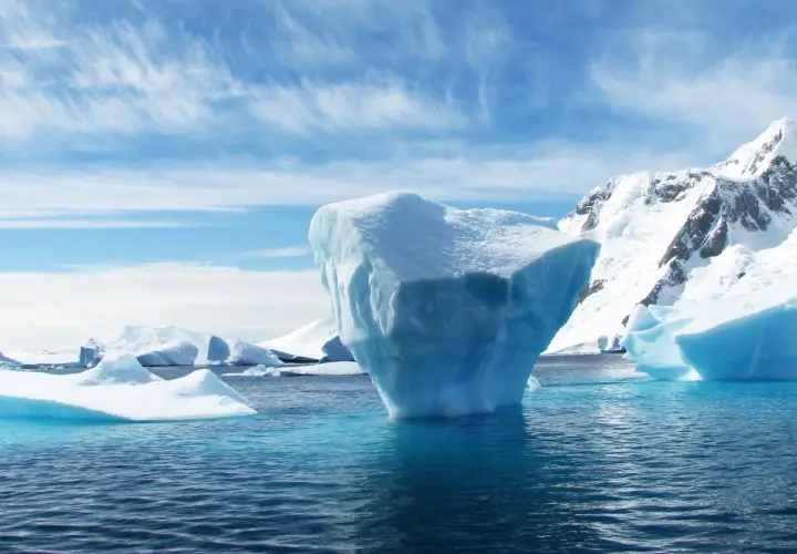 Eisberge im Meer, eine Anomalie des Wassers, vor schneebedeckten Bergen unter einem blauen Himmel mit Federwolken.