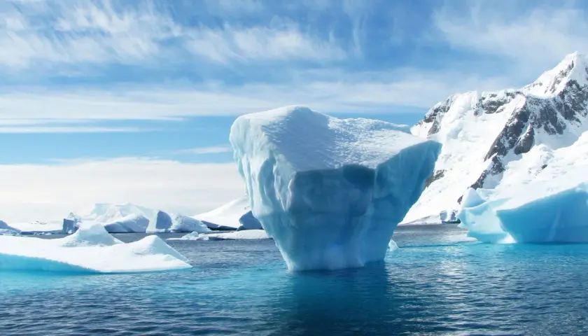 Eisberge im Meer, eine Anomalie des Wassers, vor schneebedeckten Bergen unter einem blauen Himmel mit Federwolken.