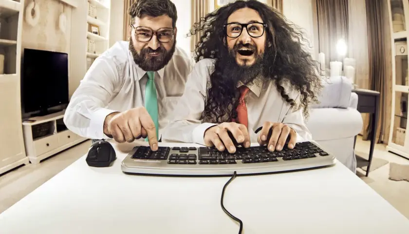 Zwei Männer mit Brillen und Krawatten tippen auf einer Tastatur.