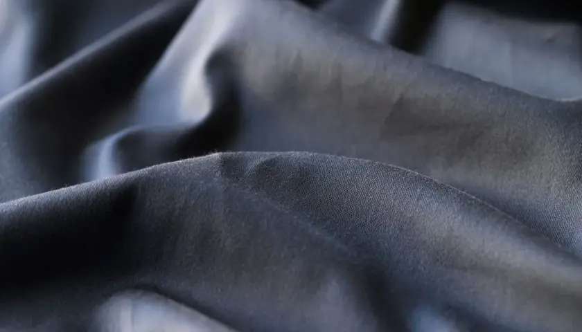 Dunkler, zerknitterter Stoff, der die Nachteile von Polyester wie Knitterbildung und mangelnde Atmungsaktivität verdeutlicht.