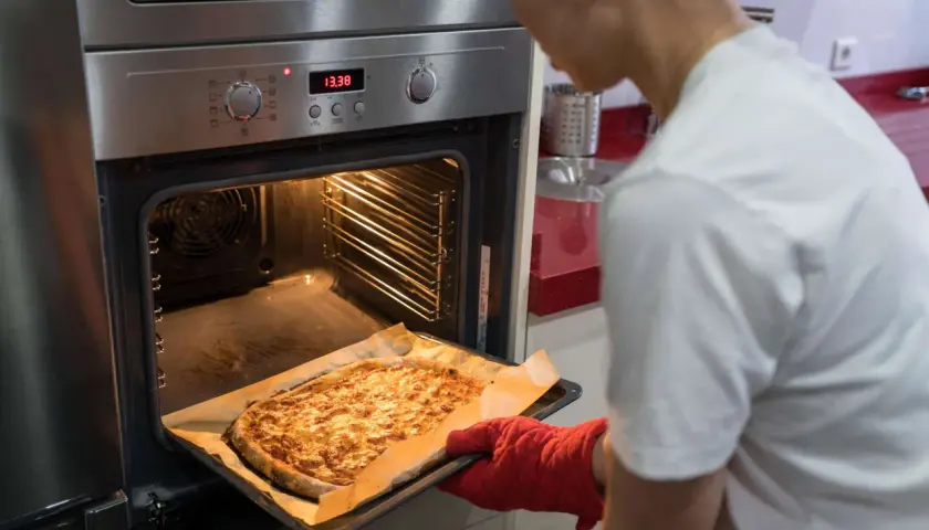 Frau holt goldbraune Pizza aus dem Ofen, der auf Ober-/Unterhitze und Umluft eingestellt ist.