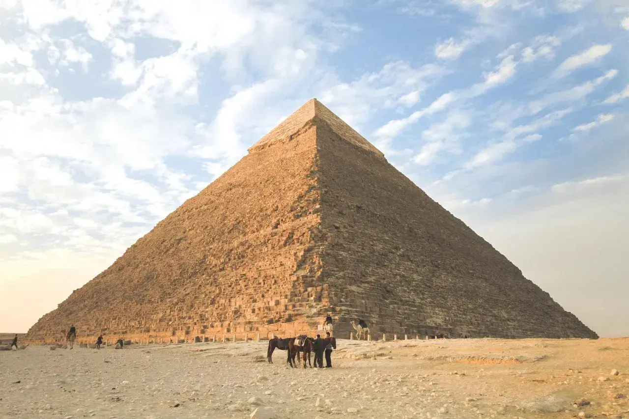 Die Pyramide von Gizeh, ein Meisterwerk geometrischer Formen im Alltag, ragt majestätisch in den Himmel. Menschen und Tiere beleben die Wüstenlandschaft.