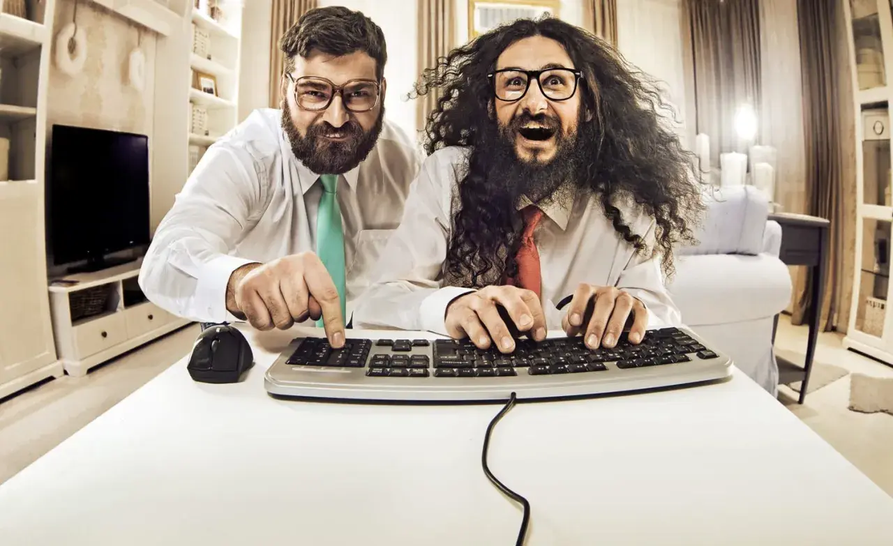 Zwei Männer mit Brillen und Krawatten tippen auf einer Tastatur.