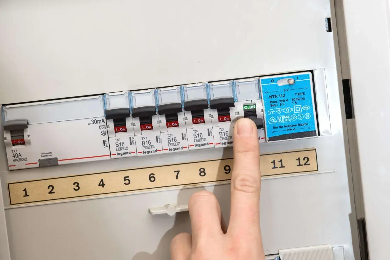 Finger drückt auf Sicherungsschalter, um eine defekte Sicherung zu erkennen. Die Nummerierung der Schalter ist sichtbar.