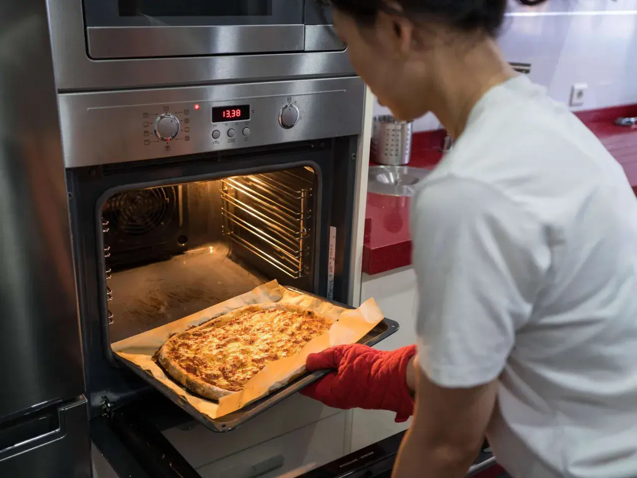 Frau holt goldbraune Pizza aus dem Ofen, der auf Ober-/Unterhitze und Umluft eingestellt ist.