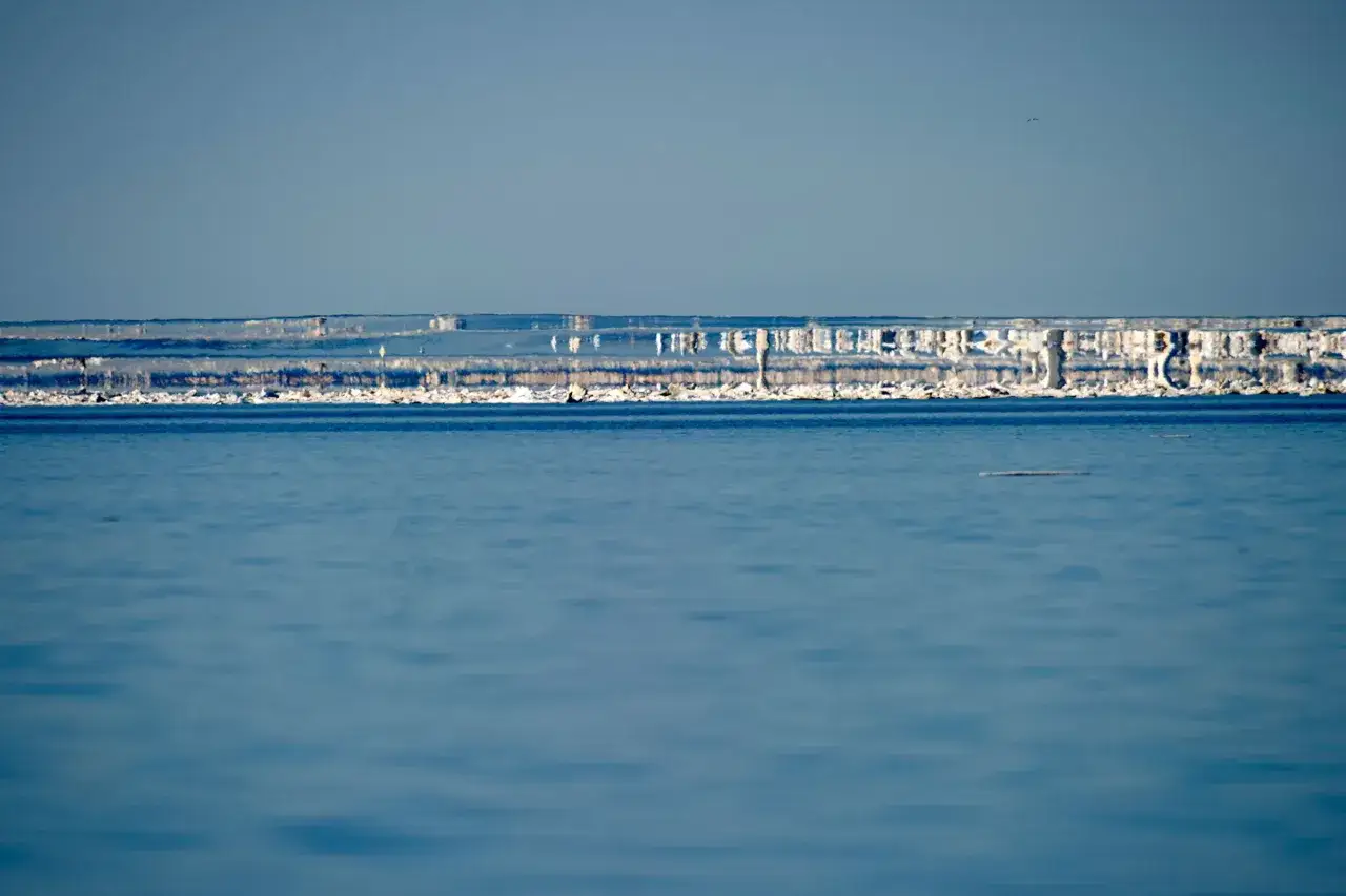 Eisformationen auf dem Wasser, die wie eine Fata Morgana wirken. Die Spiegelung und Verzerrung erzeugt eine surreale Szenerie.