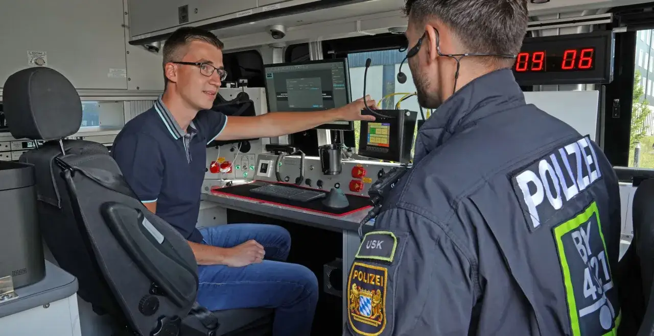 Zwei M&auml;nner im Inneren eines Polizeifahrzeugs, einer erkl&auml;rt dem anderen die Technik. Ein spannender Einblick in den Polizeiberuf.