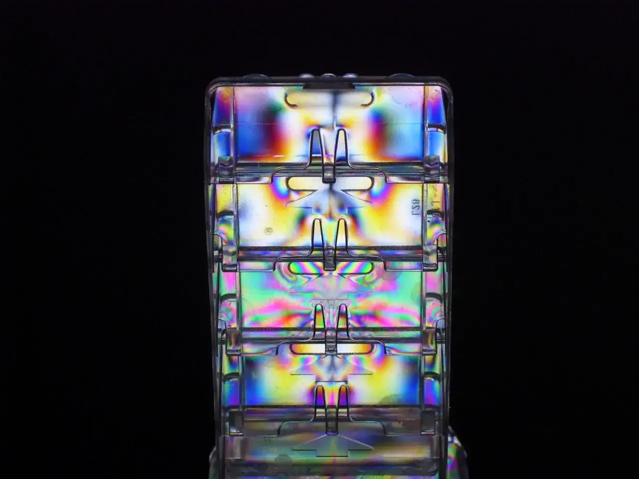 Strukturierte Kunststoffteile, beleuchtet mit polarisiertem Licht, zeigen ein Kaleidoskop aus Farben und Mustern.