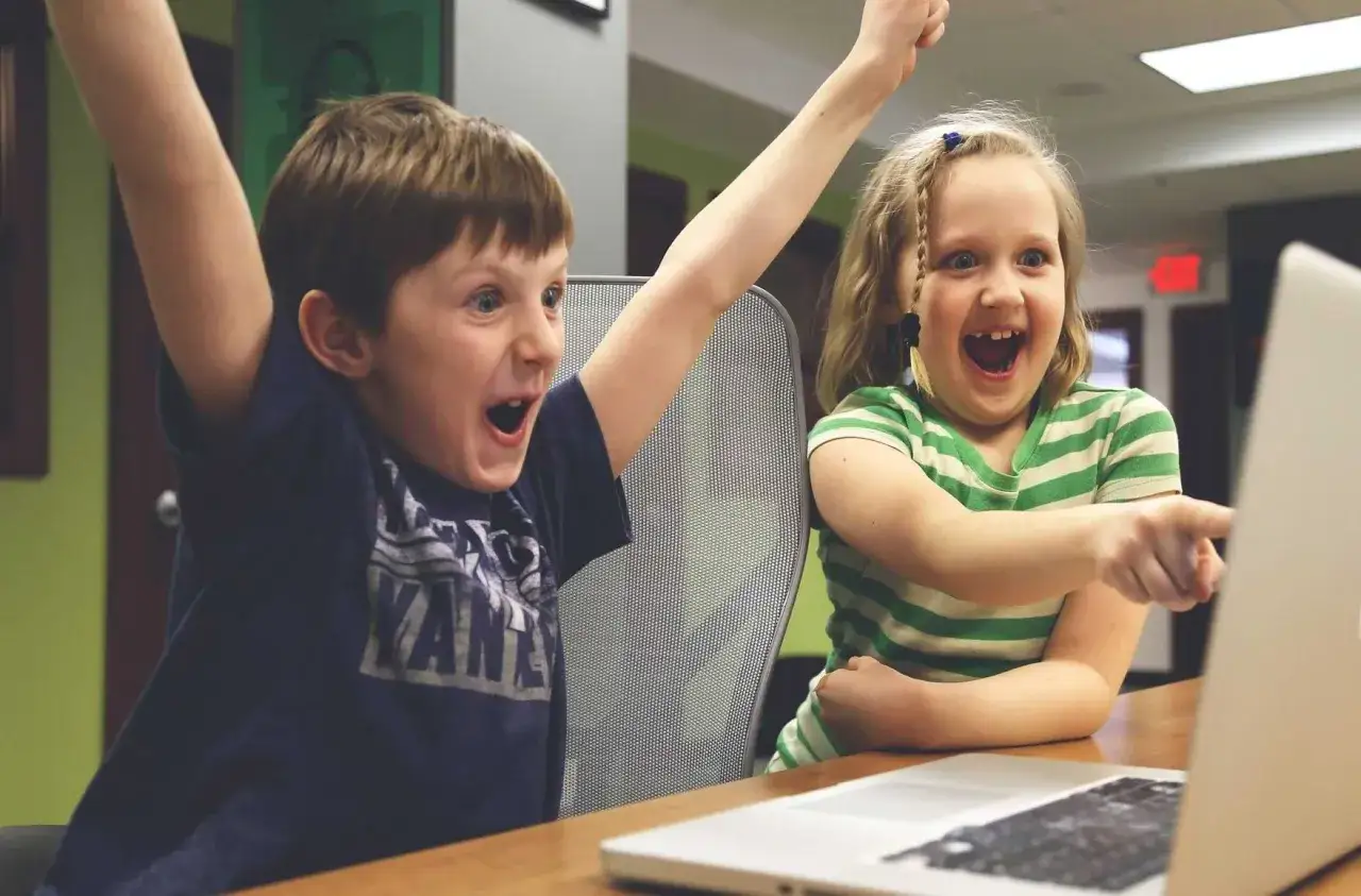 Zwei Kinder jubeln vor einem Laptop. Sie lernen, was ist coden, und sind begeistert von ihren Erfolgen.