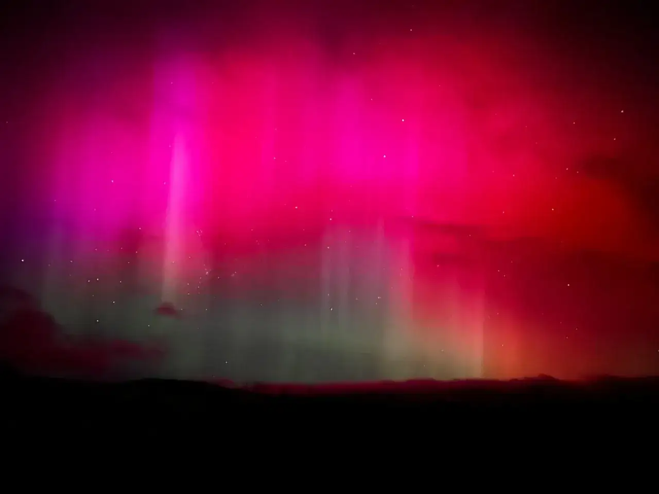 Spektakul&auml;re Polarlichter in Pink und Rot leuchten &uuml;ber einer dunklen Landschaft. So entstehen Polarlichter durch Sonnenwind.
